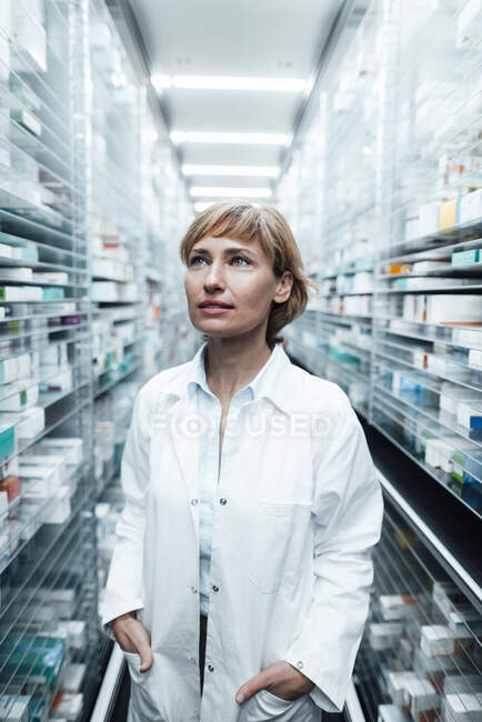 Farmacista donna con le mani in tasca guardando altrove mentre si trovava nel negozio di farmacia — Foto stock