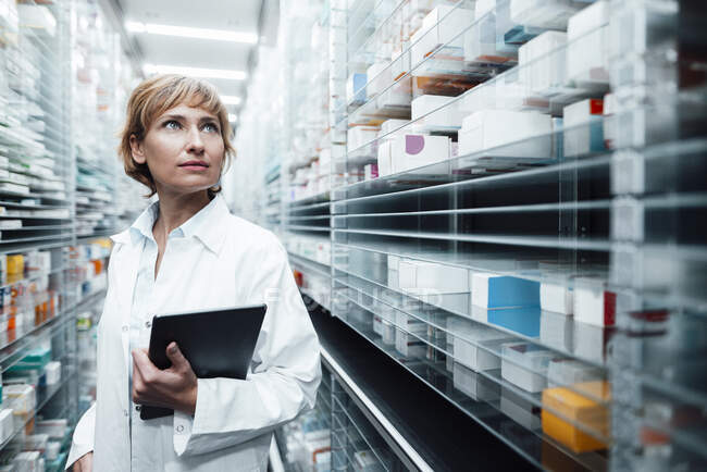 Farmacista femminile con tablet digitale che cerca medicina nel negozio di medicina — Foto stock