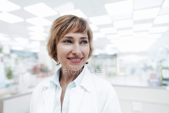 Farmacéutica rubia mirando hacia otro lado mientras está parada en la farmacia - foto de stock
