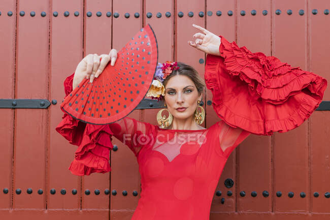 Танцівниця фламенко з фаном руки танцює перед червоними дверима. — стокове фото