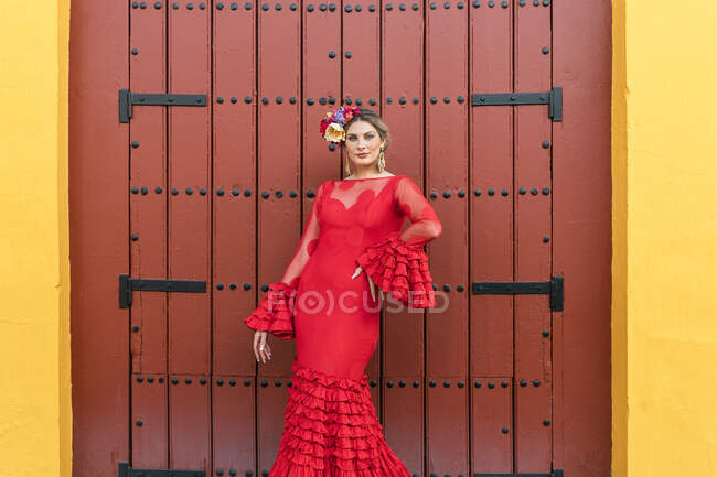 Жінка в сукні фламенко стоїть з рукою на стегні перед дверима. — стокове фото