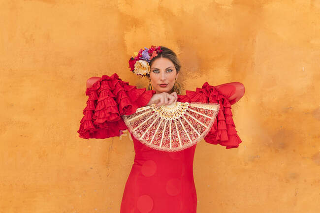 Femmina artista flamenco tenendo ventilatore mano mentre in piedi di fronte alla parete arancione — Foto stock