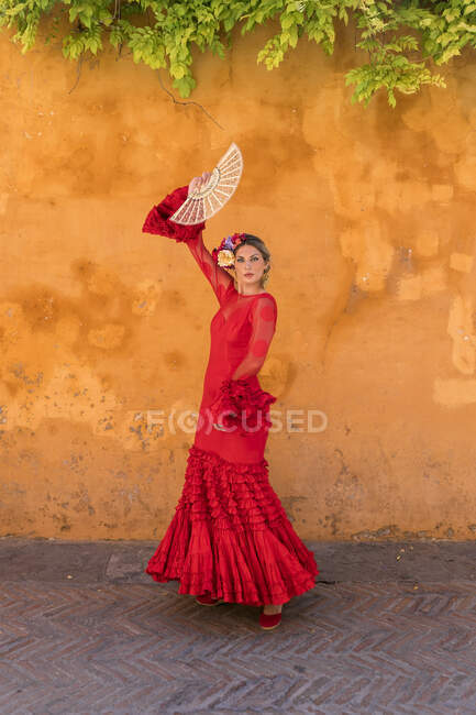 Female dancer with hand fan dancing in front of orange wall — Stock Photo