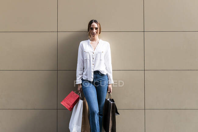 Улыбающаяся женщина, стоящая с пакетами для покупок у стены — стоковое фото