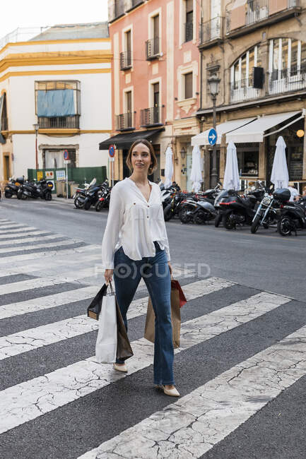 Giovane donna con borse della spesa che cammina su strada in città — Foto stock
