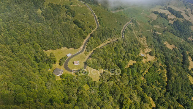 Aerial panorama of forested mountain ridge and secluded huts along hairpin curve of winding country road — Stock Photo