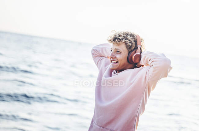 Усміхнений молодий чоловік з руками за голову слухає музику в сонячний день — стокове фото