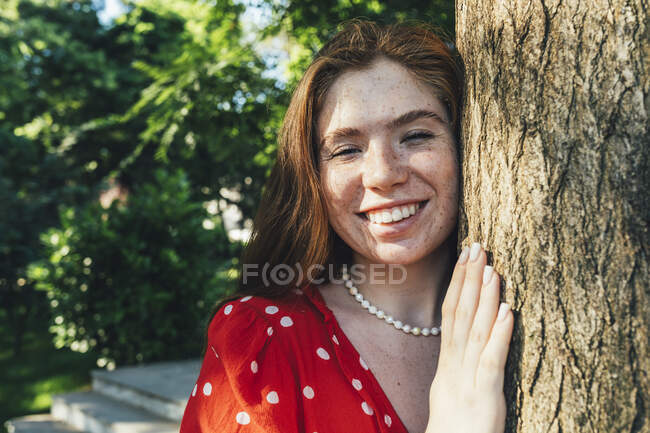 Joyeux jeune femme par tronc d'arbre dans le parc — Photo de stock