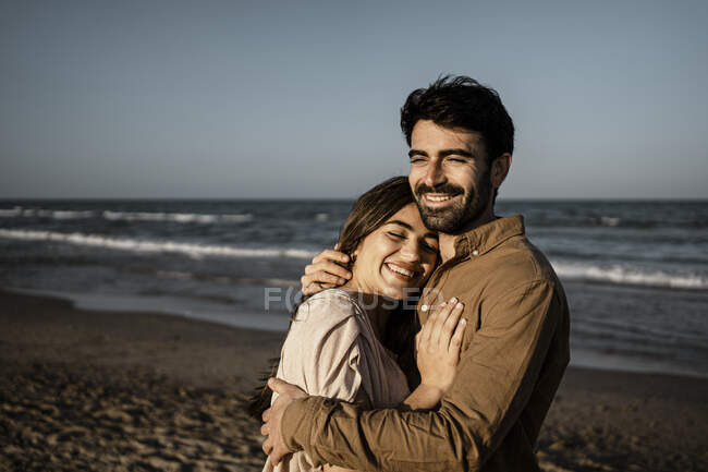 Joyeux jeune couple embrassant tout en se tenant à la plage — Photo de stock
