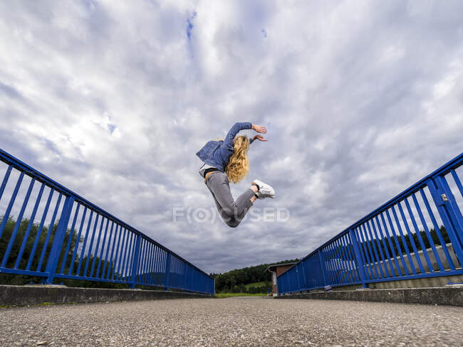 Junge Frau springt gegen wolkenverhangenen Himmel über Remsbrücke — Stockfoto