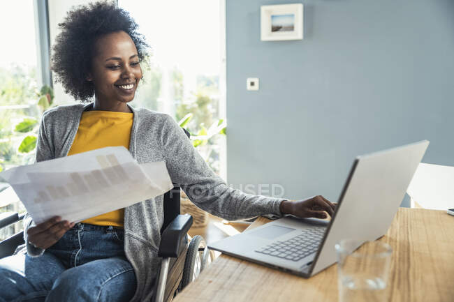 Young female freelancer holding document while working on laptop at home office — Stock Photo