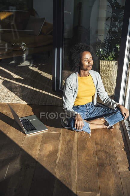 Woman with eyes closed meditating while sitting on floor at home — Stock Photo
