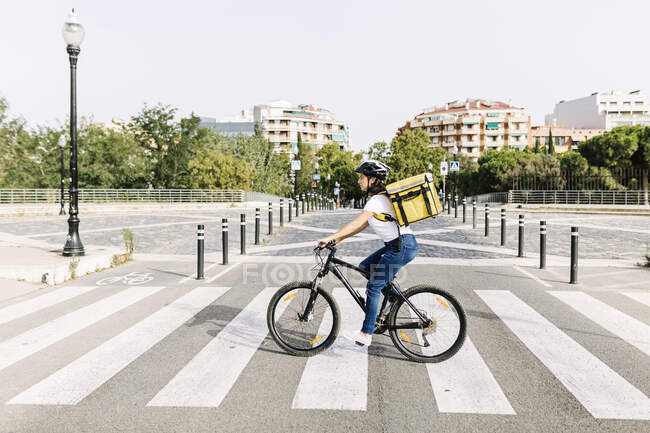 Entrega mujer que lleva bolsa de mensajero mientras monta bicicleta en el camino - foto de stock