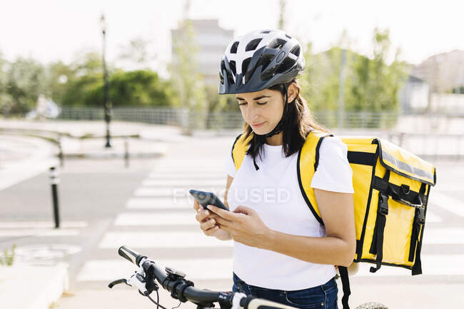 Mulher de entrega usando telefone celular enquanto está de pé na estrada — Fotografia de Stock