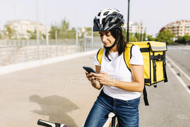 Entrega feminina com bicicleta usando telefone celular no dia ensolarado — Fotografia de Stock