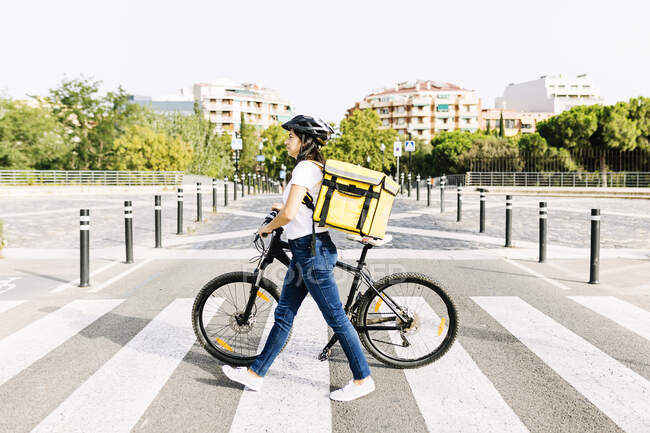 Mulher de entrega com mochila bicicleta de rodas na estrada durante o dia ensolarado — Fotografia de Stock
