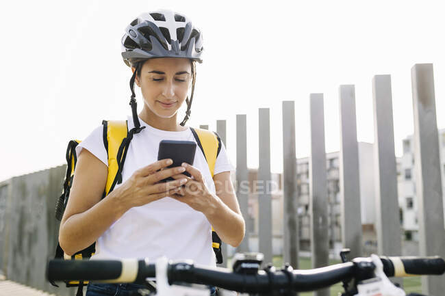Entrega feminina com bicicleta usando telefone celular — Fotografia de Stock