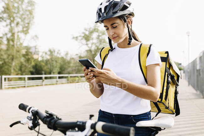 Entrega feminina usando telefone celular em pé de bicicleta na estrada — Fotografia de Stock