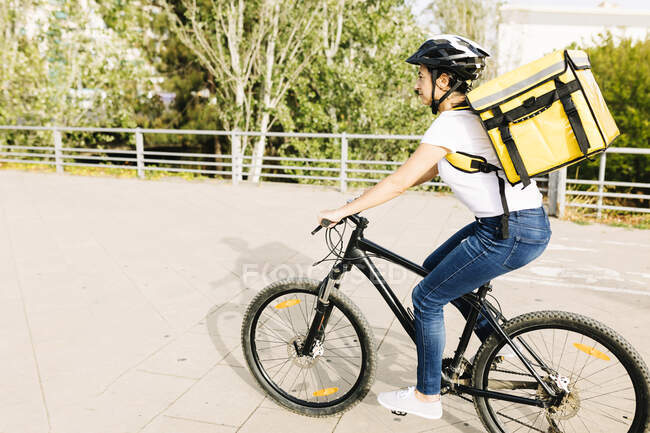 Mulher entrega pessoa com capacete e mochila andar de bicicleta na estrada — Fotografia de Stock