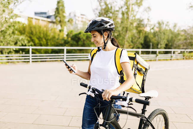 Mulher de parto sorridente usando telefone celular enquanto roda de bicicleta — Fotografia de Stock