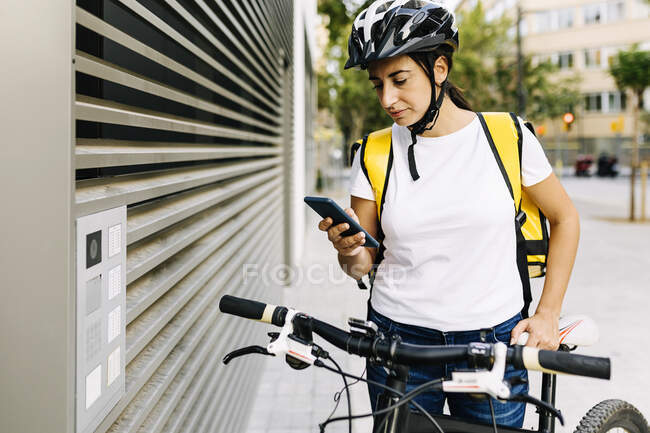 Pessoa de entrega feminina usando telefone celular em pé por portão — Fotografia de Stock