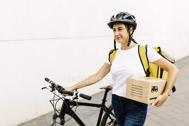 Entrega feminina pessoa segurando pacote enquanto caminha com bicicleta no caminho — Fotografia de Stock