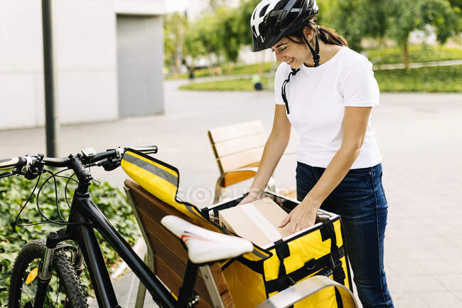 Mulher de entrega removendo correio da mochila no banco de bicicleta — Fotografia de Stock