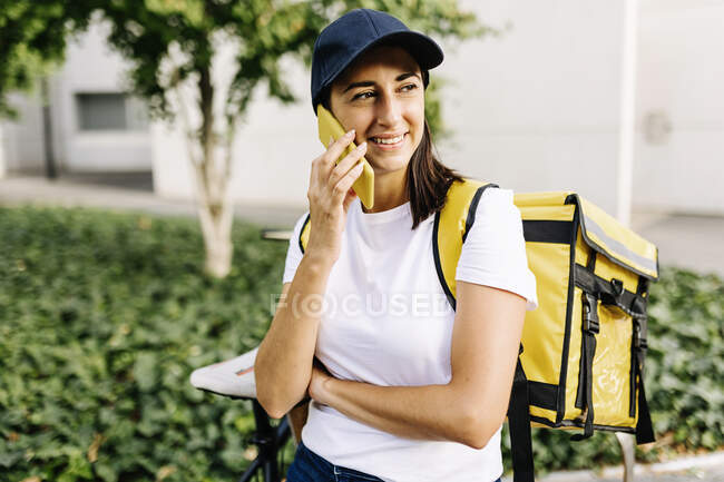 Donna di servizio essenziale sorridente con lo zaino di consegna che parla sul telefono cellulare — Foto stock