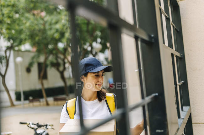 Entrega feminina pessoa segurando pacote enquanto está em pé no portão — Fotografia de Stock