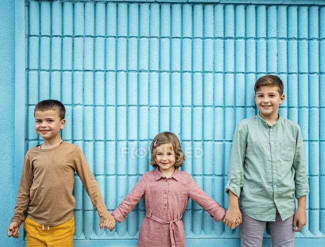 Frères et sœurs tenant la main debout devant le mur bleu — Photo de stock
