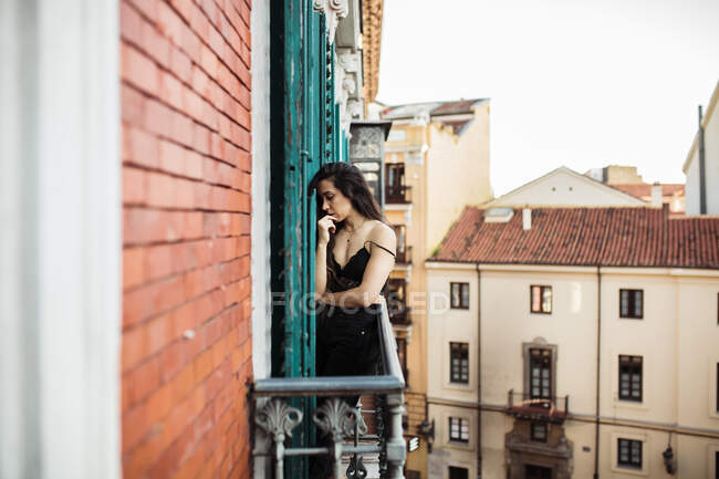 Грустная женщина с рукой на подбородке стоит на балконе — стоковое фото