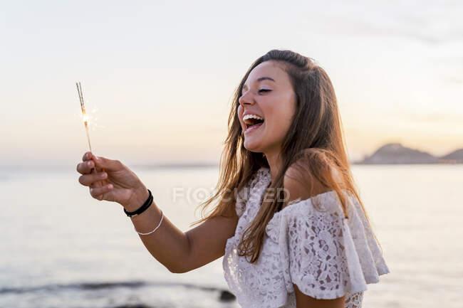 Веселая молодая женщина, держащая искру на пляже — стоковое фото