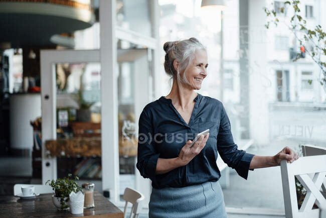 Donna d'affari con telefono cellulare in piedi al tavolo del caffè — Foto stock