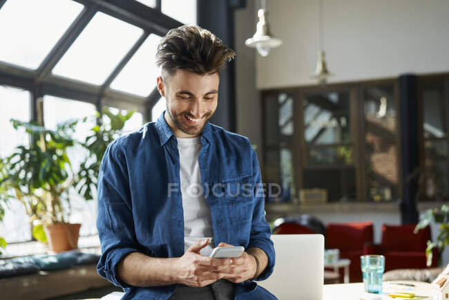 Happy young male professional smiling while using smart phone in office — Stock Photo