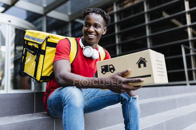 Happy delivery man holding box while sitting on steps — Stock Photo