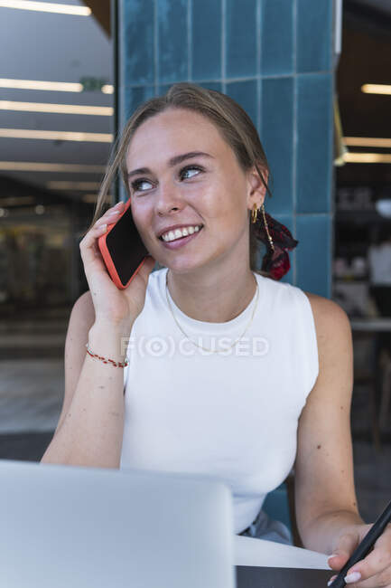 Lächelnde Geschäftsfrau telefoniert, während sie mit Laptop im Café sitzt — Stockfoto