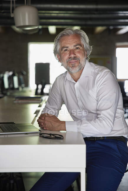 Mature male professional sitting with hands clasped at desk in office — Stock Photo
