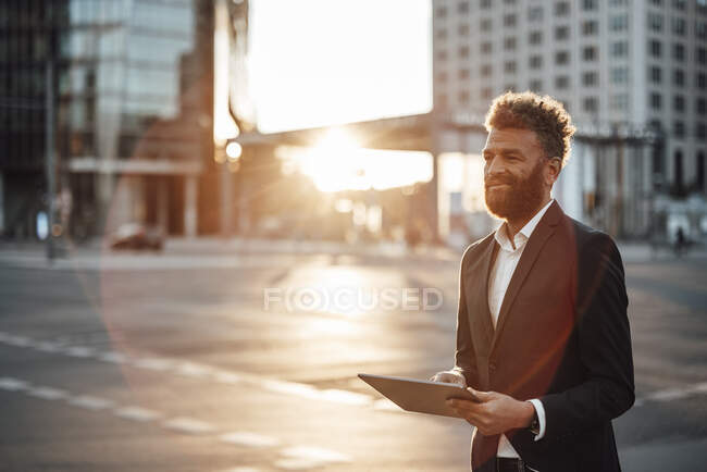 Зрелый бизнесмен улыбается, держа цифровой планшет на улице — стоковое фото