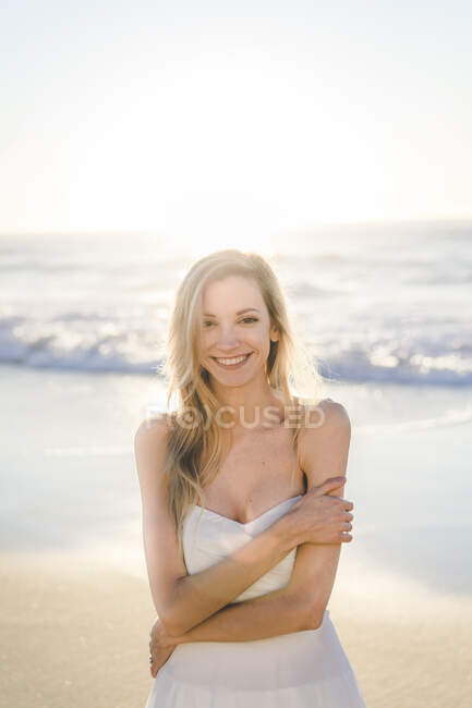 Smiling bride hugging self on beach during sunrise — Stock Photo