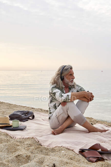 Uomo che abbraccia le ginocchia mentre ascolta musica in spiaggia — Foto stock