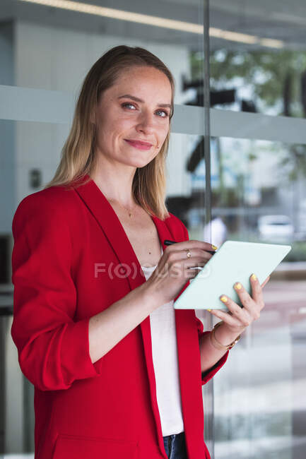 Geschäftsfrau mit digitalem Tablet steht vor Glaswand — Stockfoto