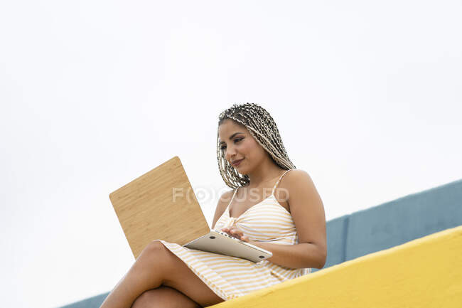 Donna che utilizza il computer portatile mentre seduto sul muro di contenimento — Foto stock
