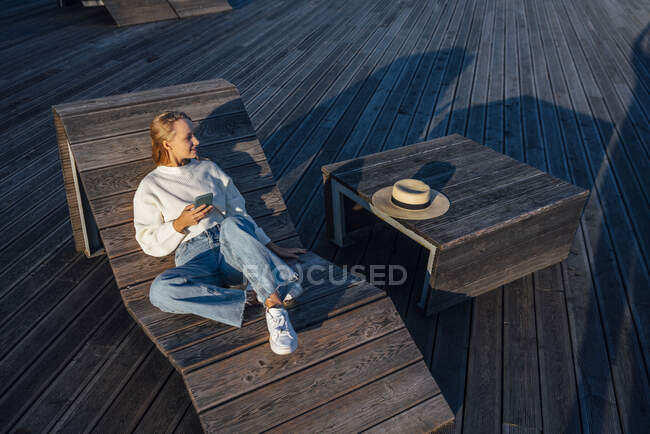 Woman with smart phone sitting on wooden bench — Stock Photo