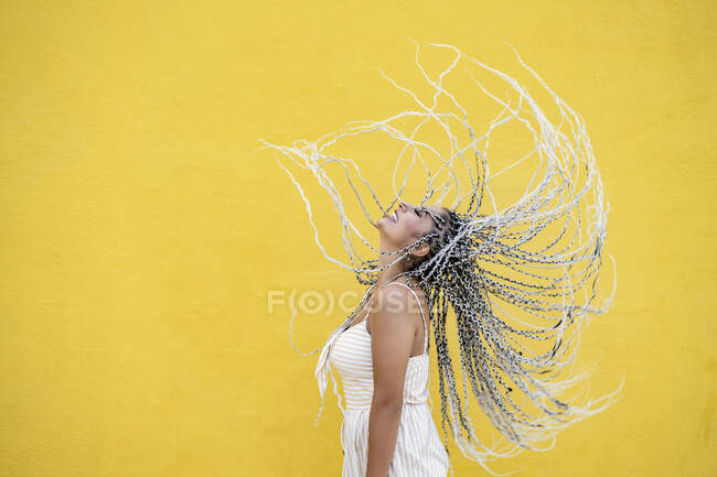 Молода жінка кидає волосся на жовту стіну — стокове фото