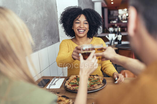 Счастливая молодая женщина поднимает тосты с друзьями-мужчинами и женщинами в ресторане — стоковое фото
