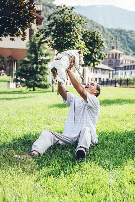 Uomo felice raccogliendo cane mentre seduto sull'erba — Foto stock