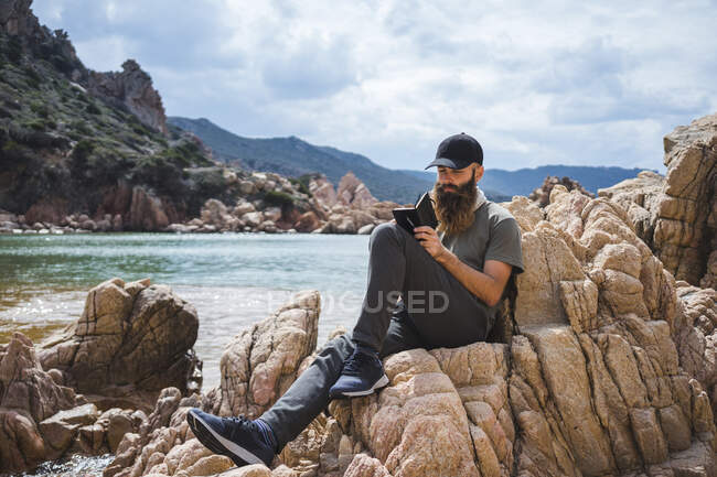 Homme écrivant dans le livre assis sur le rocher — Photo de stock