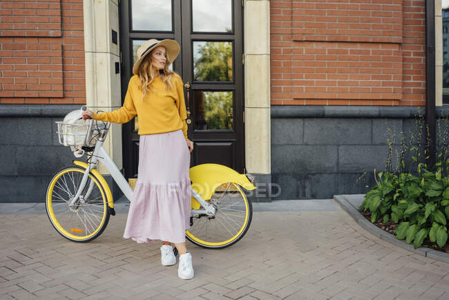 Jeune femme avec vélo debout devant le bâtiment — Photo de stock