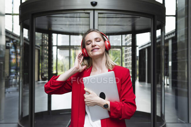 Donna d'affari che tiene il computer portatile mentre ascolta musica attraverso cuffie con gli occhi chiusi — Foto stock