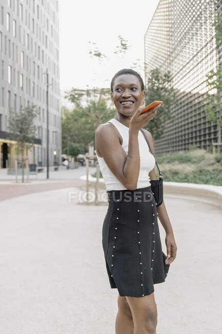 Freelance sorridente che invia messaggi vocali tramite smartphone in città — Foto stock